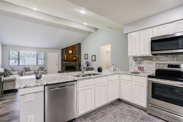 kitchen with vaulted ceiling with beams, kitchen peninsula, white cabinets, a brick fireplace, and appliances with stainless steel finishes