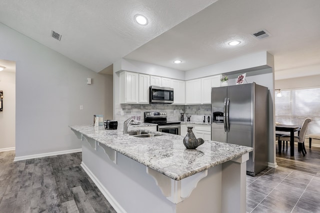 kitchen with a kitchen breakfast bar, kitchen peninsula, sink, white cabinetry, and appliances with stainless steel finishes