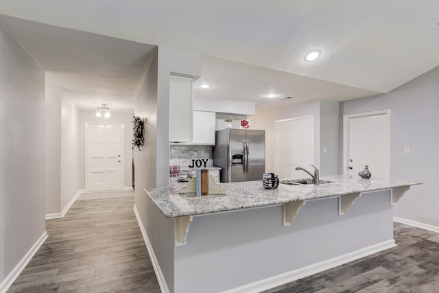 kitchen featuring sink, stainless steel fridge, white cabinets, light stone counters, and hardwood / wood-style flooring