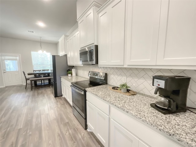 kitchen featuring light stone counters, white cabinets, decorative light fixtures, appliances with stainless steel finishes, and light wood-type flooring