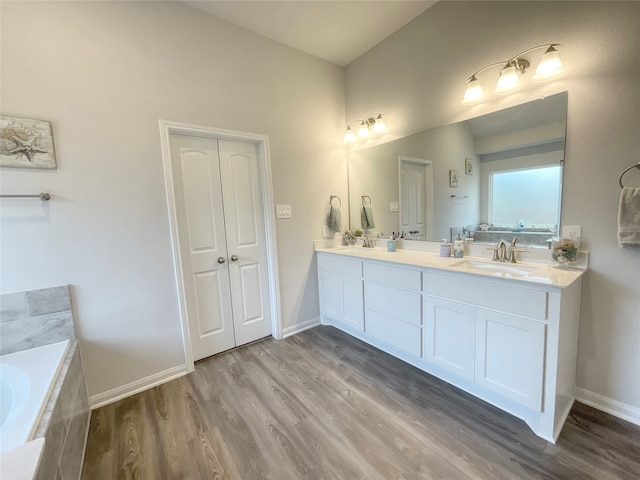 bathroom with a relaxing tiled tub, vanity, and hardwood / wood-style floors