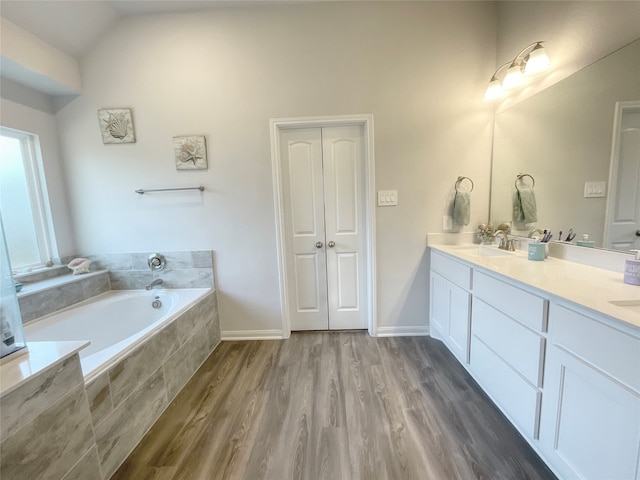 bathroom featuring hardwood / wood-style floors, lofted ceiling, a relaxing tiled tub, and vanity