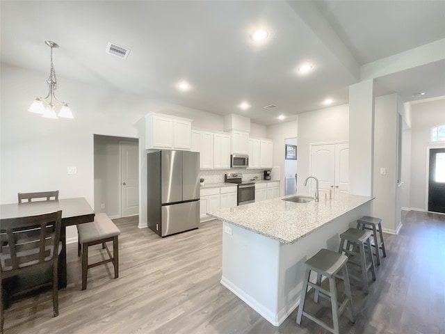 kitchen with an island with sink, stainless steel appliances, sink, white cabinetry, and light hardwood / wood-style flooring