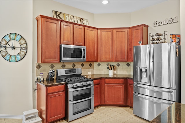 kitchen with appliances with stainless steel finishes, decorative backsplash, light tile patterned flooring, and dark stone counters