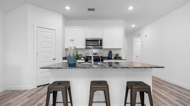 kitchen with white cabinetry, stainless steel appliances, a kitchen breakfast bar, light hardwood / wood-style flooring, and a kitchen island with sink