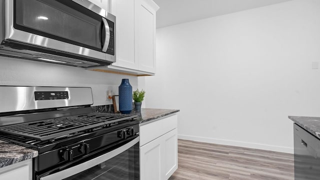 kitchen with white cabinets, appliances with stainless steel finishes, light hardwood / wood-style floors, and dark stone counters