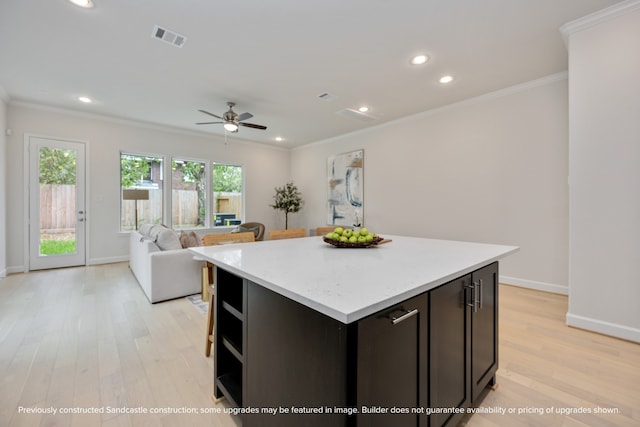 kitchen with light wood-type flooring, crown molding, ceiling fan, and a center island