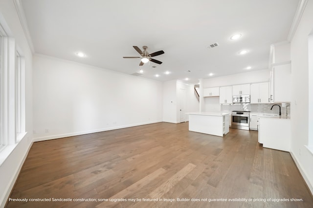 unfurnished living room with wood-type flooring, ornamental molding, sink, and ceiling fan