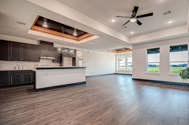 kitchen featuring hanging light fixtures, backsplash, wood-type flooring, a tray ceiling, and a center island