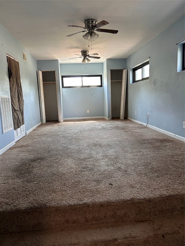 unfurnished bedroom featuring two closets, carpet flooring, and ceiling fan