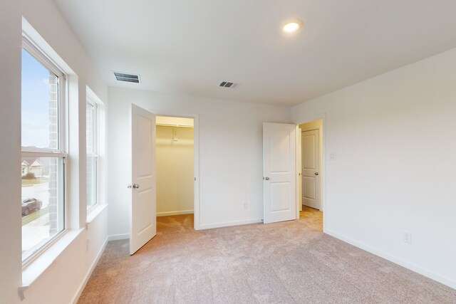 unfurnished bedroom featuring a closet, light carpet, and a walk in closet