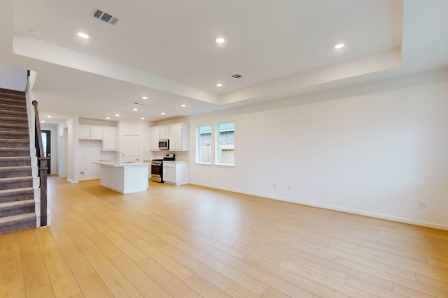 unfurnished living room with light hardwood / wood-style floors, sink, and a raised ceiling