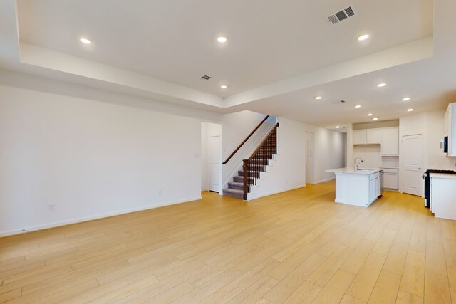 unfurnished living room featuring sink, light hardwood / wood-style flooring, and a raised ceiling