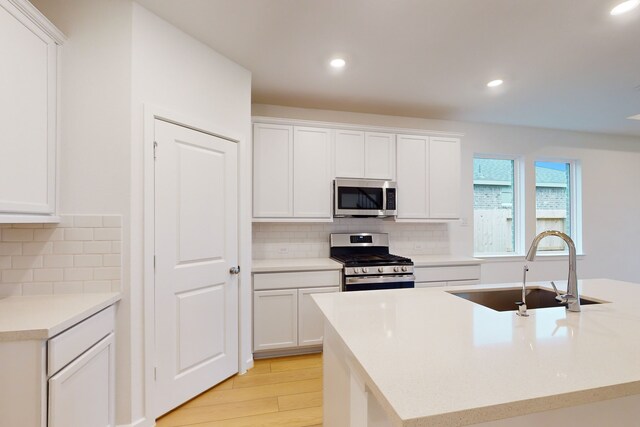 kitchen featuring light hardwood / wood-style flooring, backsplash, sink, white cabinets, and appliances with stainless steel finishes