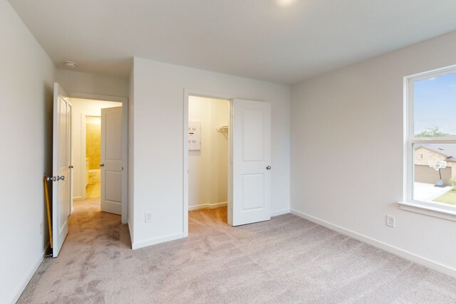 unfurnished bedroom with a walk in closet, multiple windows, a closet, and light colored carpet