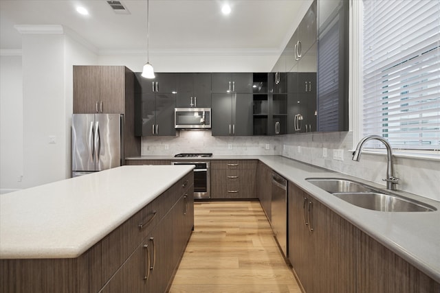 kitchen featuring stainless steel appliances, sink, ornamental molding, hanging light fixtures, and light hardwood / wood-style flooring