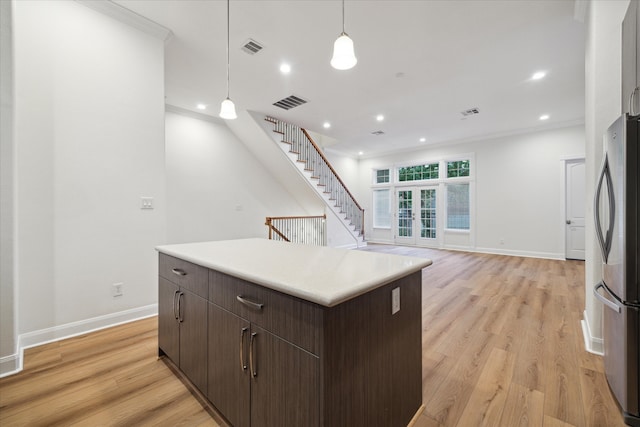 kitchen with hanging light fixtures, crown molding, dark brown cabinets, light wood-type flooring, and stainless steel fridge