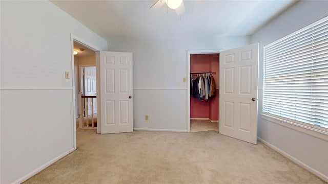 unfurnished bedroom featuring light carpet, a walk in closet, ceiling fan, multiple windows, and a closet