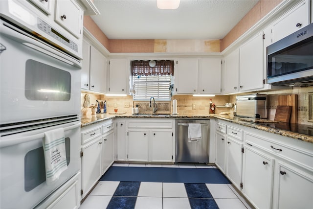 kitchen with white cabinets, tasteful backsplash, light stone countertops, sink, and stainless steel appliances