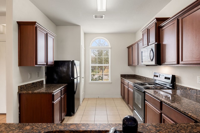 kitchen featuring stainless steel range oven, light tile patterned floors, dark stone countertops, and black fridge