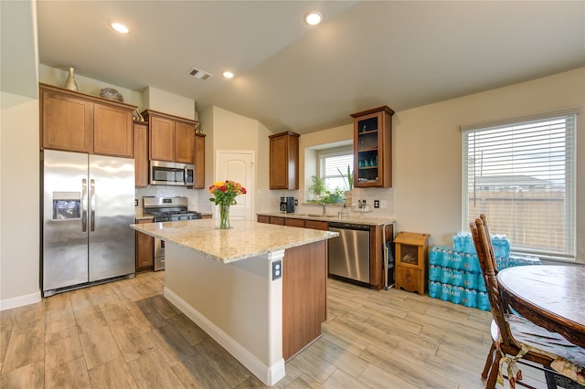 kitchen with a center island, stainless steel appliances, lofted ceiling, light stone counters, and light hardwood / wood-style flooring