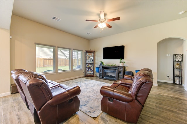 living room with a fireplace, light wood-type flooring, and ceiling fan