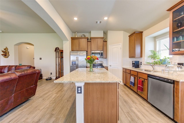 2446 Wembley Way, Rosenberg, TX 77471 - kitchen featuring appliances with stainless steel finishes, open floor plan, a sink, arched walkways, and a center island