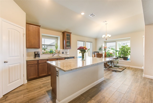 kitchen featuring light stone countertops, light wood-type flooring, sink, decorative light fixtures, and a center island