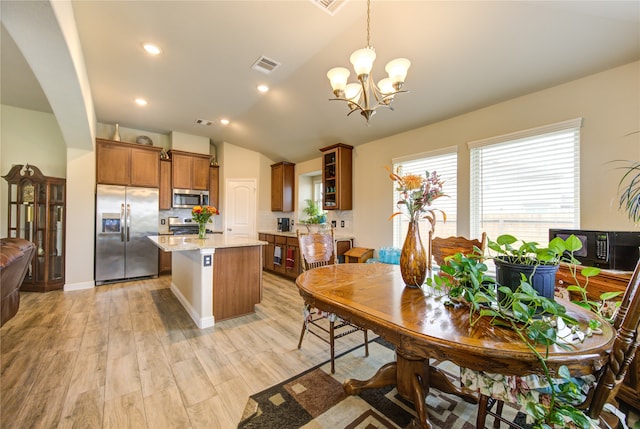 dining area with light hardwood / wood-style floors, a notable chandelier, and vaulted ceiling