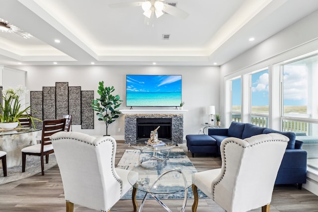 living room featuring a raised ceiling, a fireplace, ceiling fan, and light hardwood / wood-style flooring