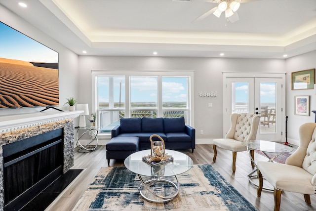 living room featuring a raised ceiling, ceiling fan, french doors, and light hardwood / wood-style floors