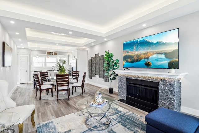 living room featuring a tray ceiling, a high end fireplace, and light hardwood / wood-style floors