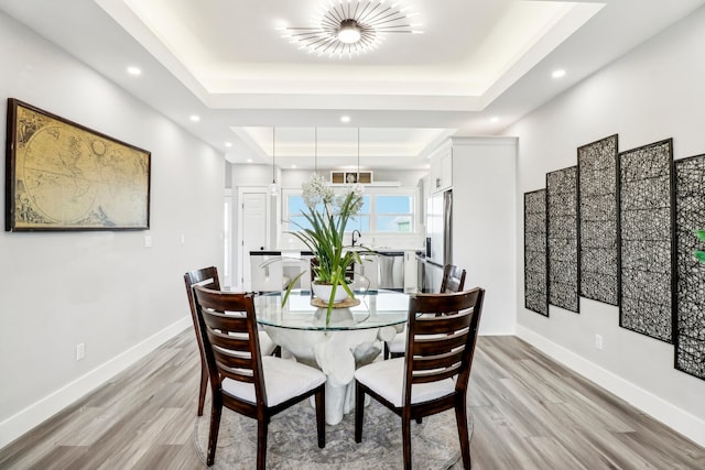 dining area with light hardwood / wood-style flooring, a raised ceiling, and sink