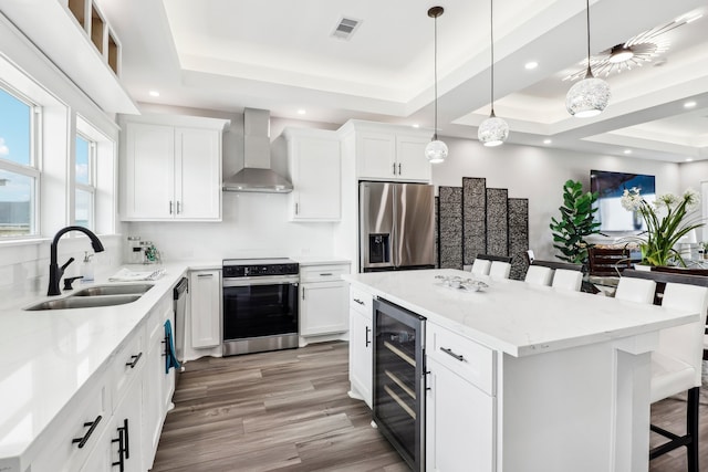 kitchen with appliances with stainless steel finishes, a tray ceiling, beverage cooler, and wall chimney range hood