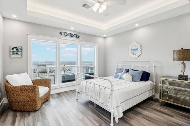 bedroom with hardwood / wood-style floors, a raised ceiling, and ceiling fan