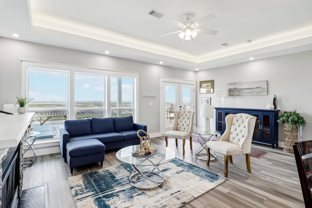 living room featuring ceiling fan, light hardwood / wood-style floors, a tray ceiling, and french doors