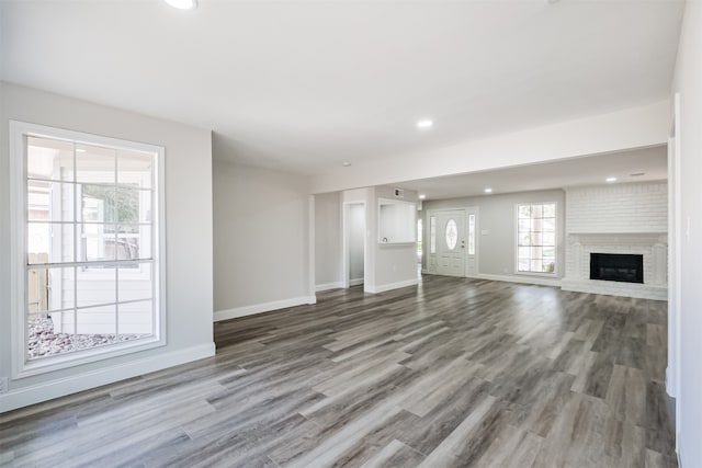 unfurnished living room featuring a healthy amount of sunlight, hardwood / wood-style flooring, and a brick fireplace