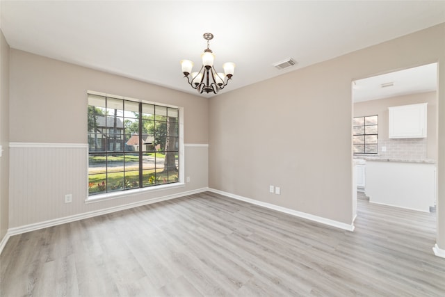 spare room with an inviting chandelier and light hardwood / wood-style floors