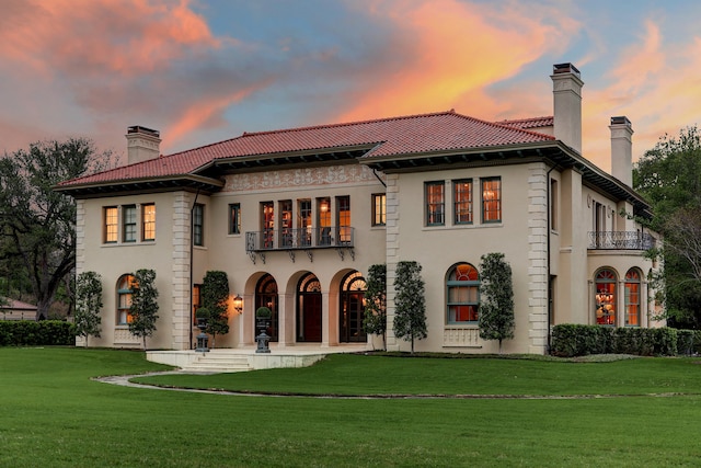 back house at dusk with a lawn and a balcony