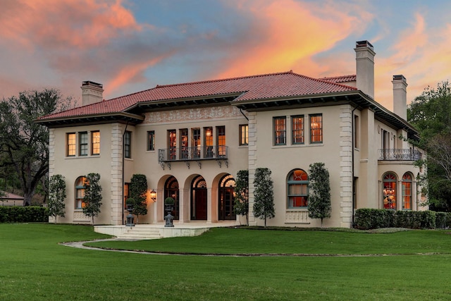 back of house with a lawn, a chimney, stucco siding, and a balcony