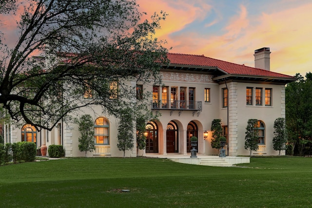 back house at dusk featuring a balcony and a lawn