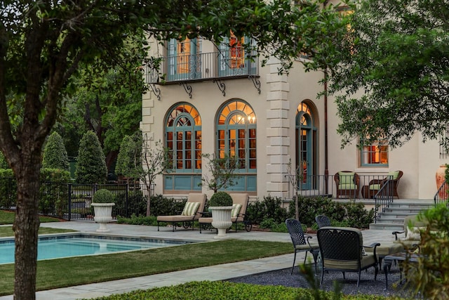 rear view of property with stucco siding, fence, an outdoor pool, and a patio