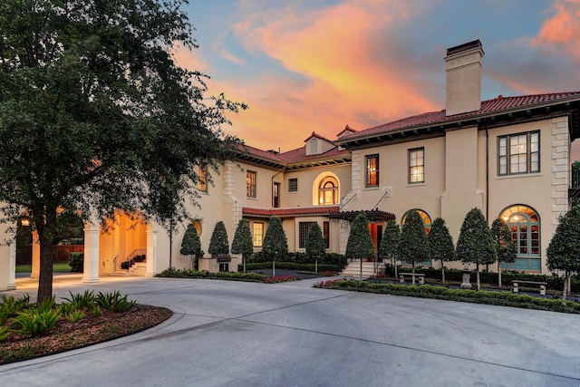 mediterranean / spanish-style home featuring a tiled roof, stucco siding, curved driveway, and a chimney