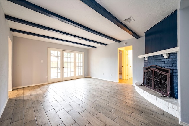 unfurnished living room featuring a textured ceiling, a brick fireplace, beamed ceiling, and light hardwood / wood-style flooring