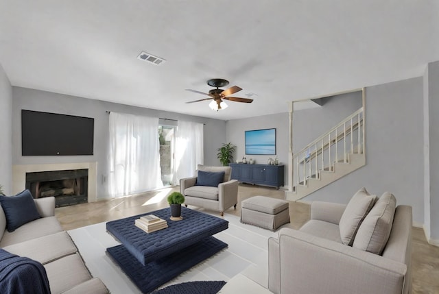 living room featuring a ceiling fan, visible vents, a fireplace, and stairs