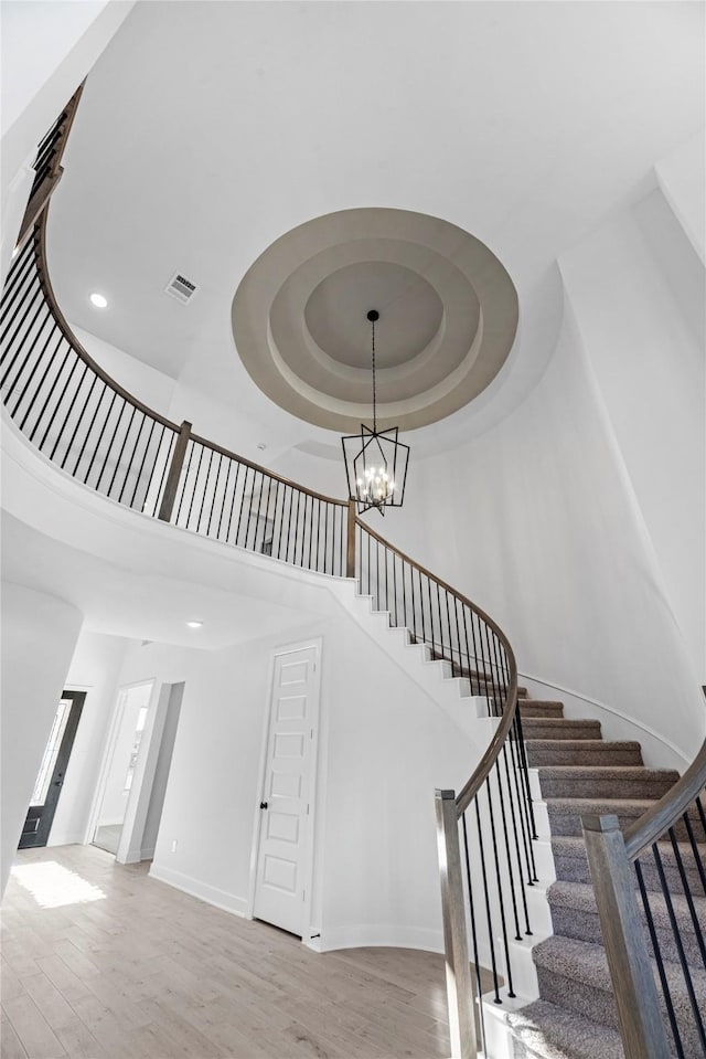 stairs featuring a raised ceiling, wood-type flooring, a high ceiling, and a chandelier