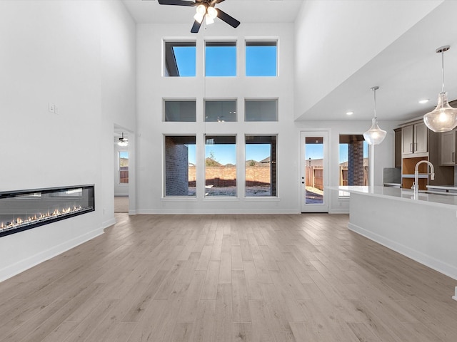 unfurnished living room featuring a high ceiling, light hardwood / wood-style floors, ceiling fan, and sink