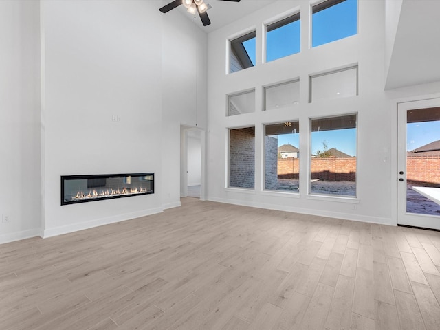 unfurnished living room with a high ceiling, light hardwood / wood-style floors, and ceiling fan