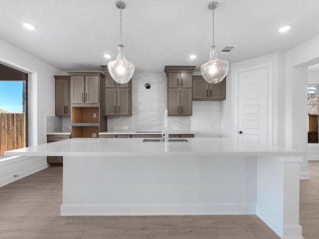 kitchen featuring a large island, sink, tasteful backsplash, decorative light fixtures, and light wood-type flooring