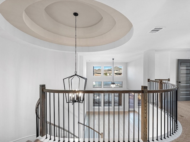 stairs with ceiling fan with notable chandelier and a tray ceiling